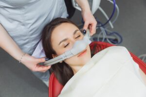 Woman with dark brown hair in dental chair with eyes closed and nitrous oxide mask over nose